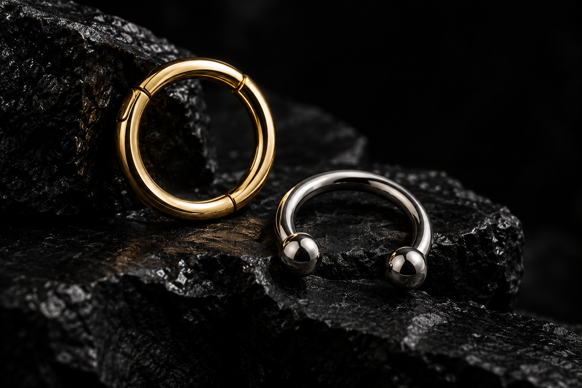 Septum clicker and hinged ring jewelry on a dark studio surface